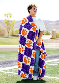 Clemson University Tigers Blanket draped around a man showcasing its vibrant purple and orange colors on a sunny field.