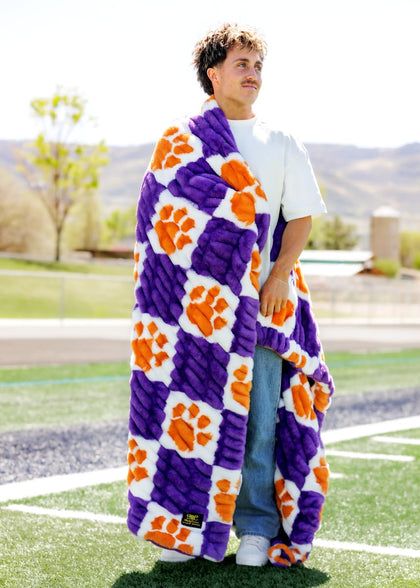 Clemson University Tigers Blanket draped around a man showcasing its vibrant purple and orange colors on a sunny field.