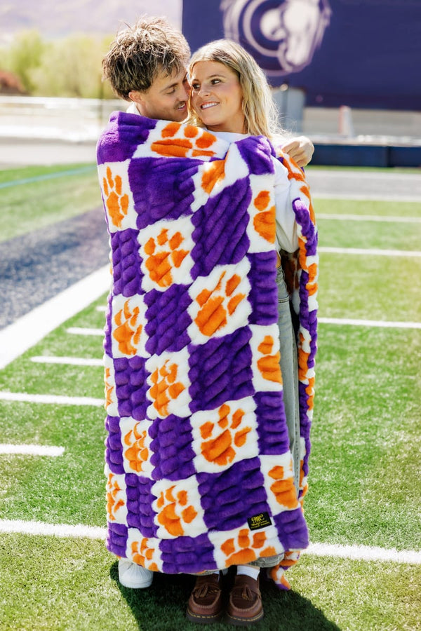 Hugs Clemson University Tigers Blanket wrapped around a person sitting on a football field with a football.