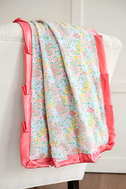 Minky Couture Dainty Floral Pastel Blanket with colorful flowers and coral satin ruffle draping over a chair.