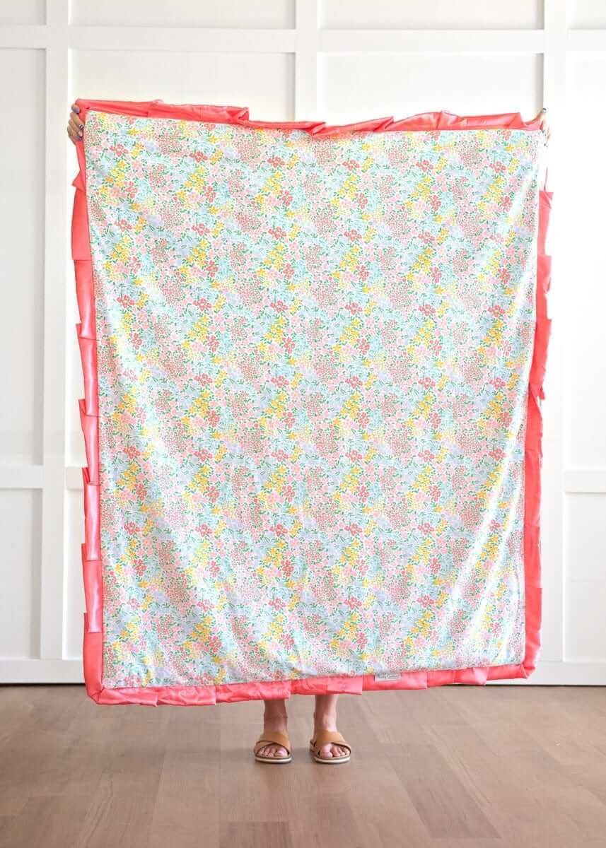 Dainty Floral Pastel Blanket featuring small yellow, pink, blue, and coral flowers on a white background with coral satin ruffle.