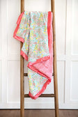 Dainty Floral Pastel Blanket displayed on a wooden ladder, featuring small colorful flowers and a coral satin ruffle.