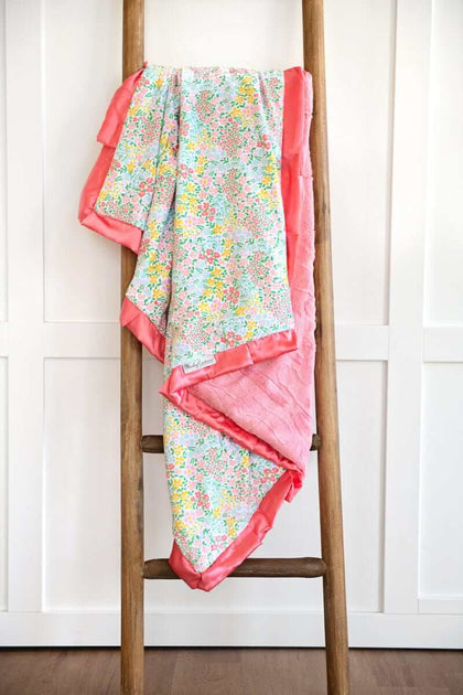 Dainty Floral Pastel Blanket displayed on a wooden ladder, featuring small colorful flowers and a coral satin ruffle.