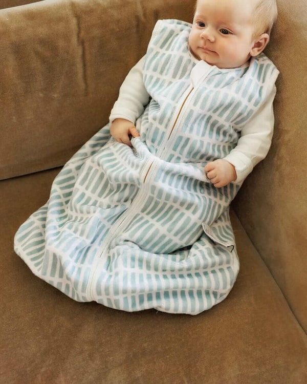 Baby lying on a light brown sofa, with Dash Wearable Minky Blanket.