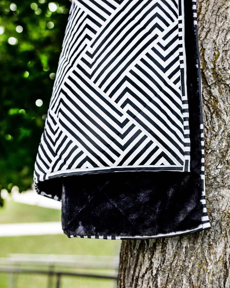 Everywhere Blanket Black Geo hanging on a tree, showcasing its geometric black pattern and plush black interior.