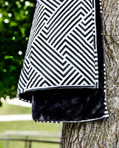 Everywhere Blanket Black Geo hanging on a tree, showcasing its geometric black pattern and plush black interior.