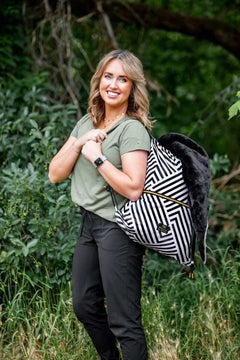 Woman smiling outdoors with Black Geo Everywhere Blanket backpack in a striped pattern against greenery.