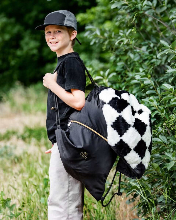 Young boy carrying Everywhere Black Blanket in a stylish drawstring bag, set against a natural outdoor background.