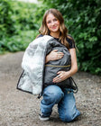 Minky Couture Charcoal Everywhere Blanket folded into a convenient pocket held by a woman outdoors.