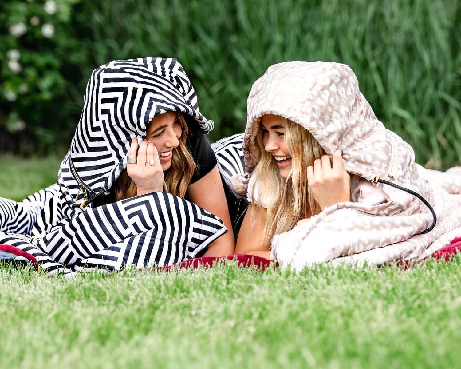 Two women laughing under the Black Geo Everywhere Blanket, enjoying their time outdoors in a grassy area.