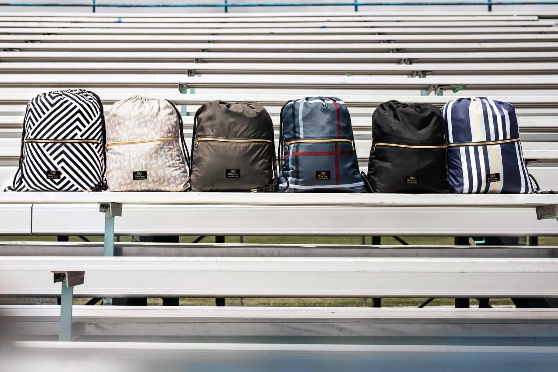 Five stylish Minky Couture backpacks displayed on bleachers in various patterns and colors.