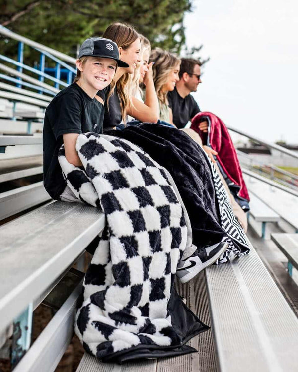 Black Everywhere Blanket used at a sports game by a group of people seated on bleachers, showcasing its cozy design.