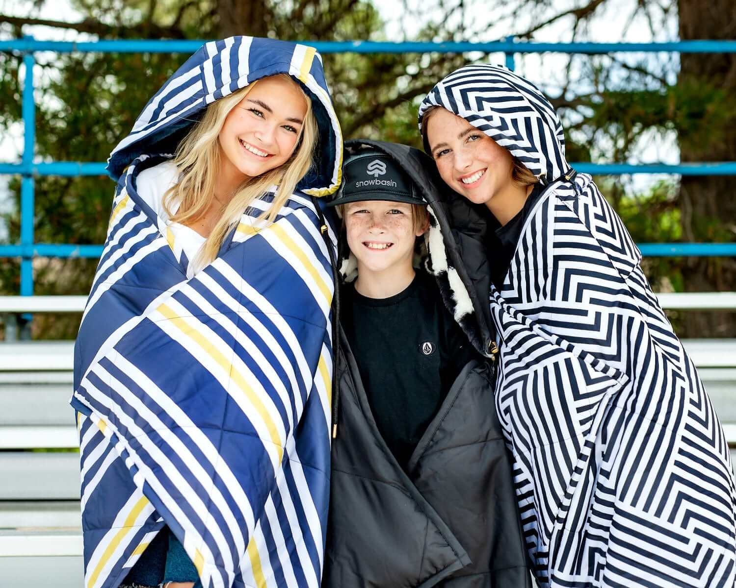 Three people wearing cozy Everywhere Blankets Black Geo, perfect for outdoor events and keeping warm.