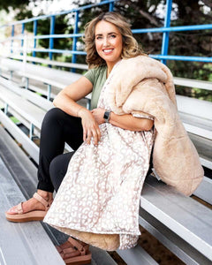 Woman sitting on bleachers with Tan Cheetah Everywhere Blanket, cozy and stylish for outdoor events.