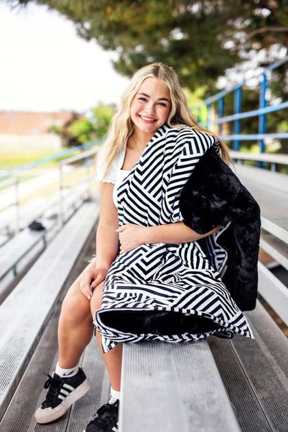 Smiling girl on bleachers wrapped in the Black Geo Everywhere Blanket, showcasing its geometric design and plush interior.