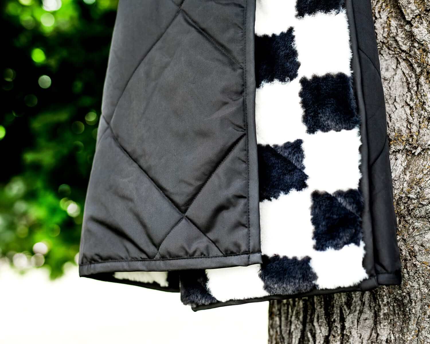 Black Everywhere Blanket hanging on a tree, showcasing solid charcoal quilted exterior and plush minky lining.