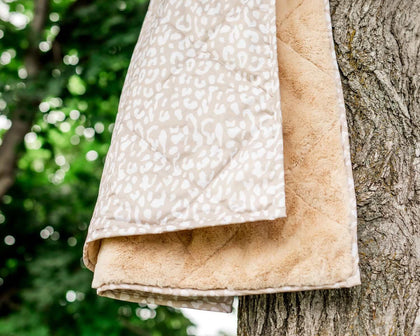 Tan Cheetah Everywhere Blanket hung on a tree, showcasing its tan cheetah outer and plush interior.