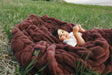 Child lying on a large warm brown Hugs Rich Mahogany Blanket in a grassy field.