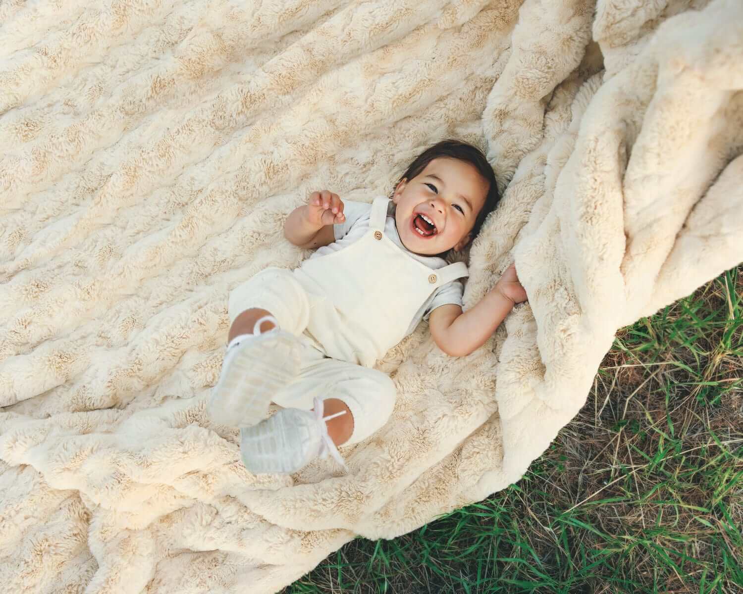 Happy child playing on the Ultra Sorbet Sand weighted blanket in a cozy outdoor setting, showcasing its soft texture.