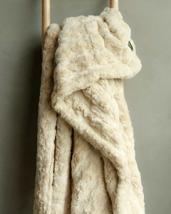 Ultra Sorbet Sand Blanket hanging on a wooden rack, showcasing its velvety-soft texture and warm tan color.