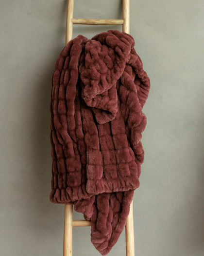 A plush warm brown Hugs Rich Mahogany Blanket draped over a wooden ladder against a gray background.