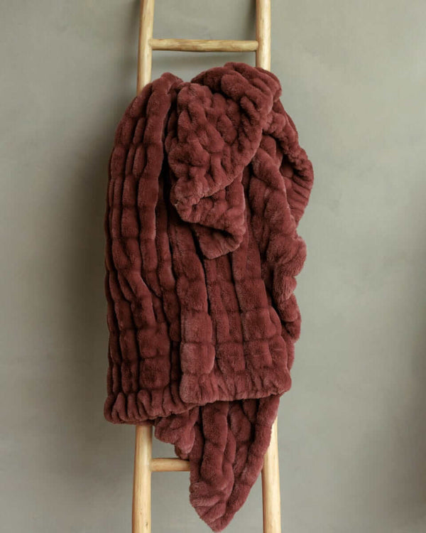 A plush warm brown Hugs Rich Mahogany Blanket draped over a wooden ladder against a gray background.