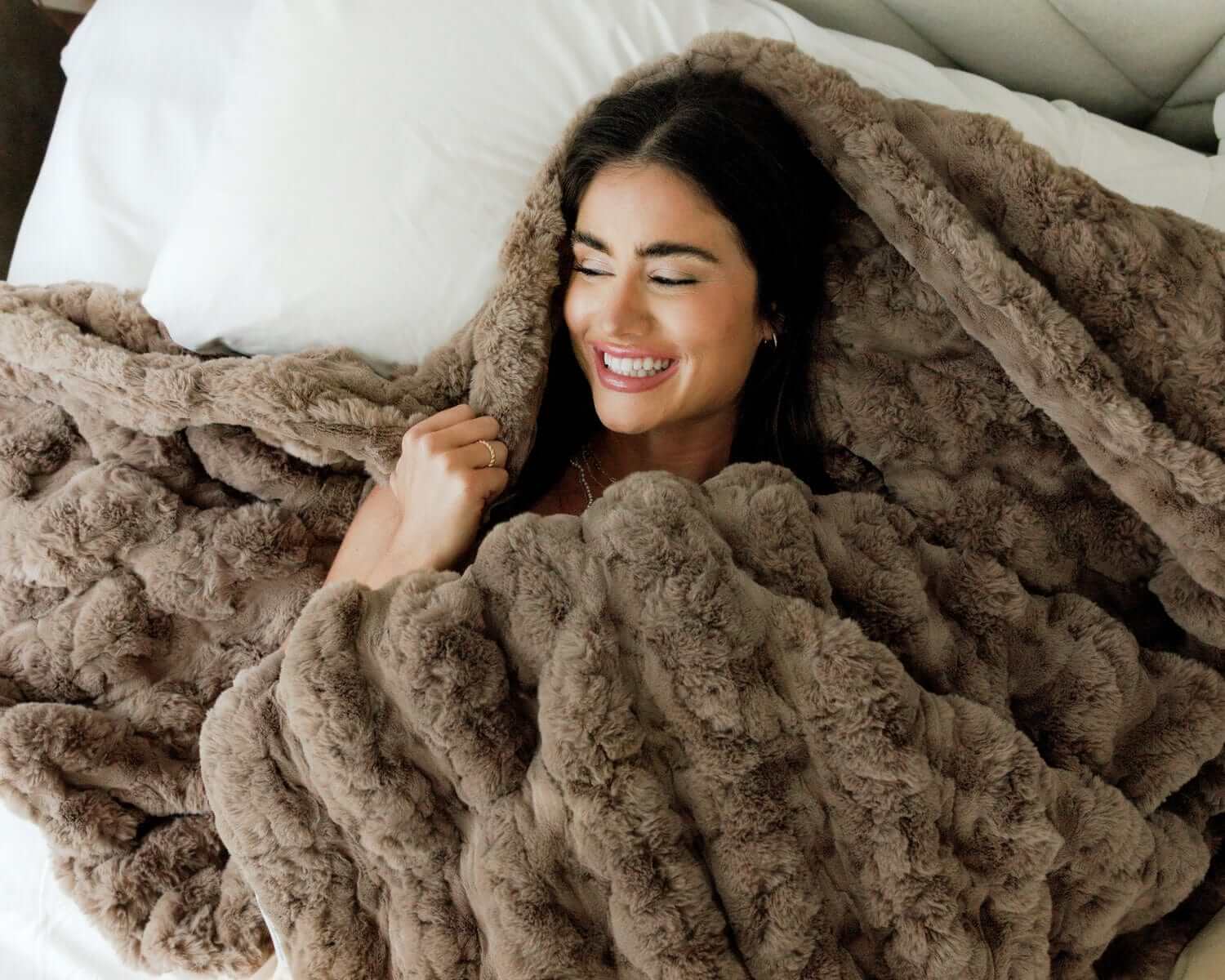 Woman smiling while wrapped in the Ultra Sorbet Gingersnap Blanket, showcasing its soft faux fur texture.