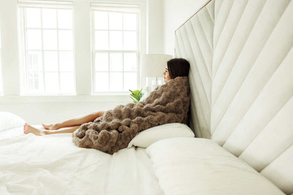 A cozy woman wrapped in the Ultra Sorbet Gingersnap Blanket, lounging on a bed with a soft faux fur texture.