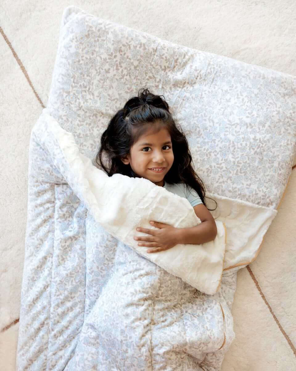 Smiling girl lying on a floral Minky Couture Forget Me Not sleeping bag.