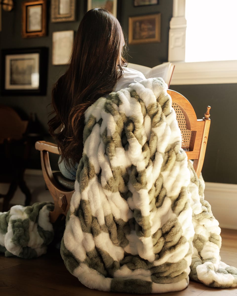 Hugs Check Sage Blanket draped over a person sitting in a chair, showcasing its plush texture and elegant design.