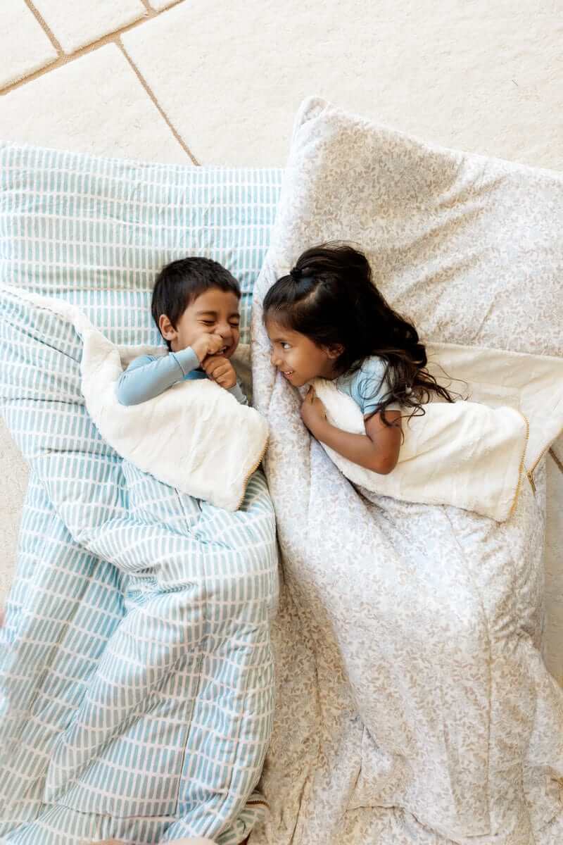 Two smiling kids laying on Minky Couture Forget Me Not sleeping bags.