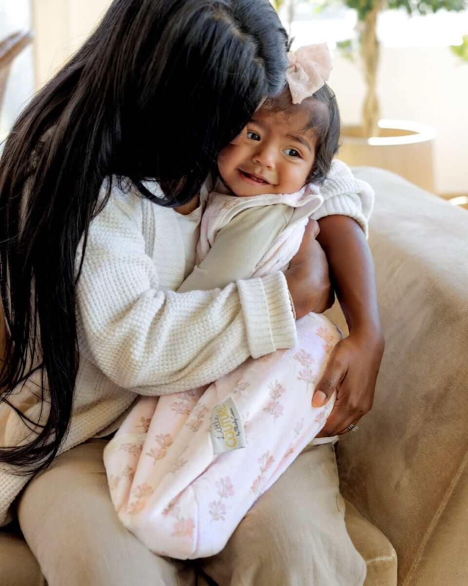 Woman carrying a baby girl with a Hampton Blooms Wearable Minky Blanket.