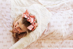 Girl with pink bows lying on a pink floral Hampton Blooms sleeping bag.