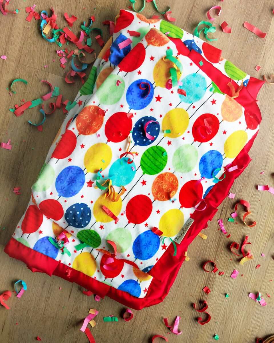 Happy Birthday Blanket featuring colorful balloons and a festive red plush backing, perfect for celebrations.