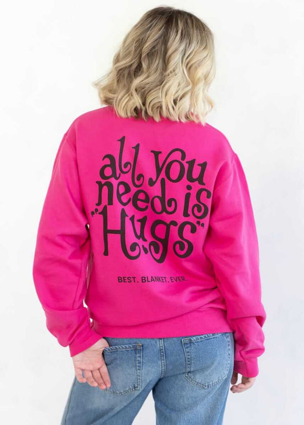 Person wearing a hot pink Minky Couture sweatshirt with “All You Need Is Hugs” text on the back.