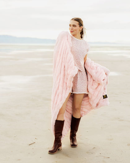 Woman standing on a beach with a pink blanket and  wearing brown boots.