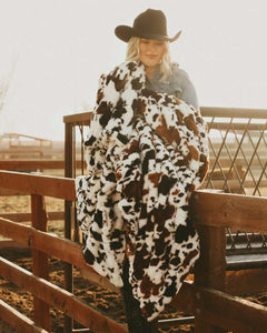 Woman holding Hugs Brown Cow faux fur blanket outdoors, featuring cow print design, perfect for cozy comfort.