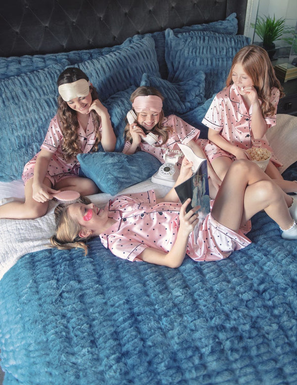 Four girls in pink pajamas sitting on a bed with blue minky couture bedding.