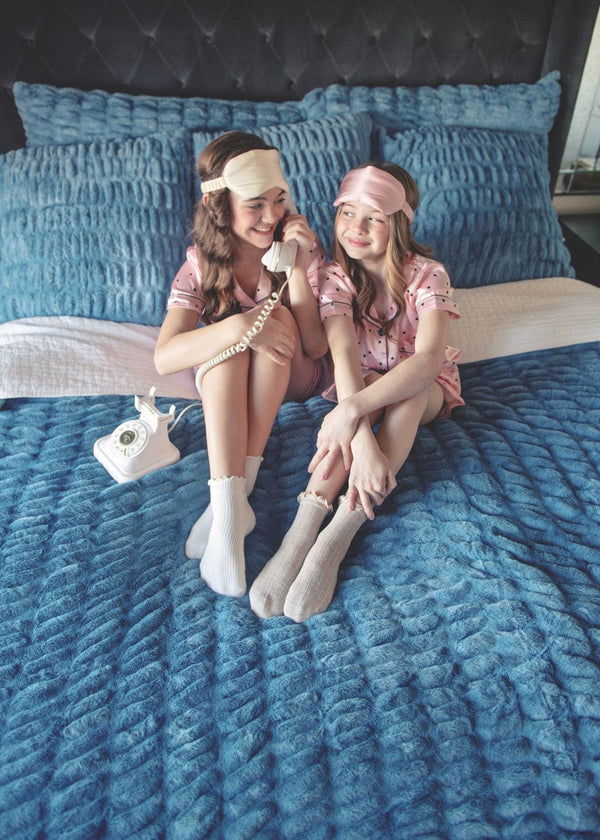 Two girls sitting on a bed with Minky Couture blue hugs bedding.