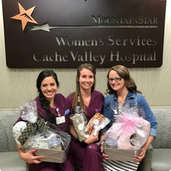 Three women in scrubs holding gift baskets in front of the MountainStar Women's Services sign at Cache Valley Hospital.