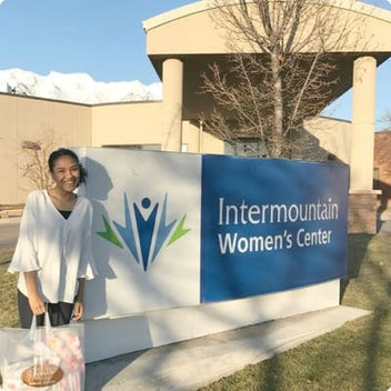 Young woman standing beside the Intermountain Women's Center sign on a sunny day.