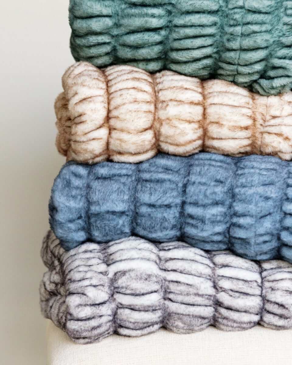 Minky Couture Hugs Blankets in a stack with different colors showcasing faux fur texture and cozy design.