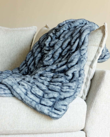 Hugs Sapphire faux fur blanket draped over a light-colored couch, showcasing its rich sapphire blue color and soft texture.
