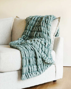 Hugs Jade faux fur blanket draped over a light-colored couch, showcasing its plush, velvety texture and elegant jade color.