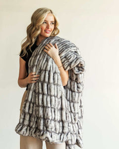 Woman draped in the Hugs Obsidian Blanket made of soft faux fur, showcasing its unique texture and warmth.