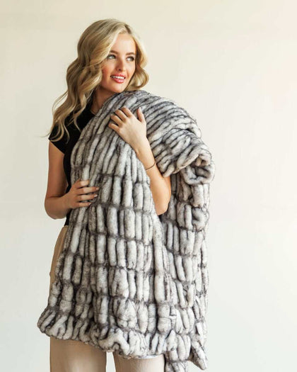 Woman draped in the Hugs Obsidian Blanket made of soft faux fur, showcasing its unique texture and warmth.