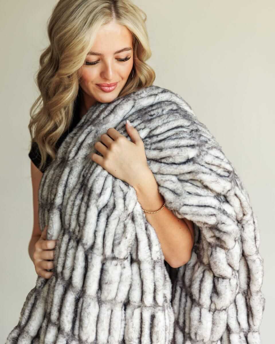 A woman enjoying the warmth of the Hugs Obsidian faux fur Blanket made from soft unique texture.
