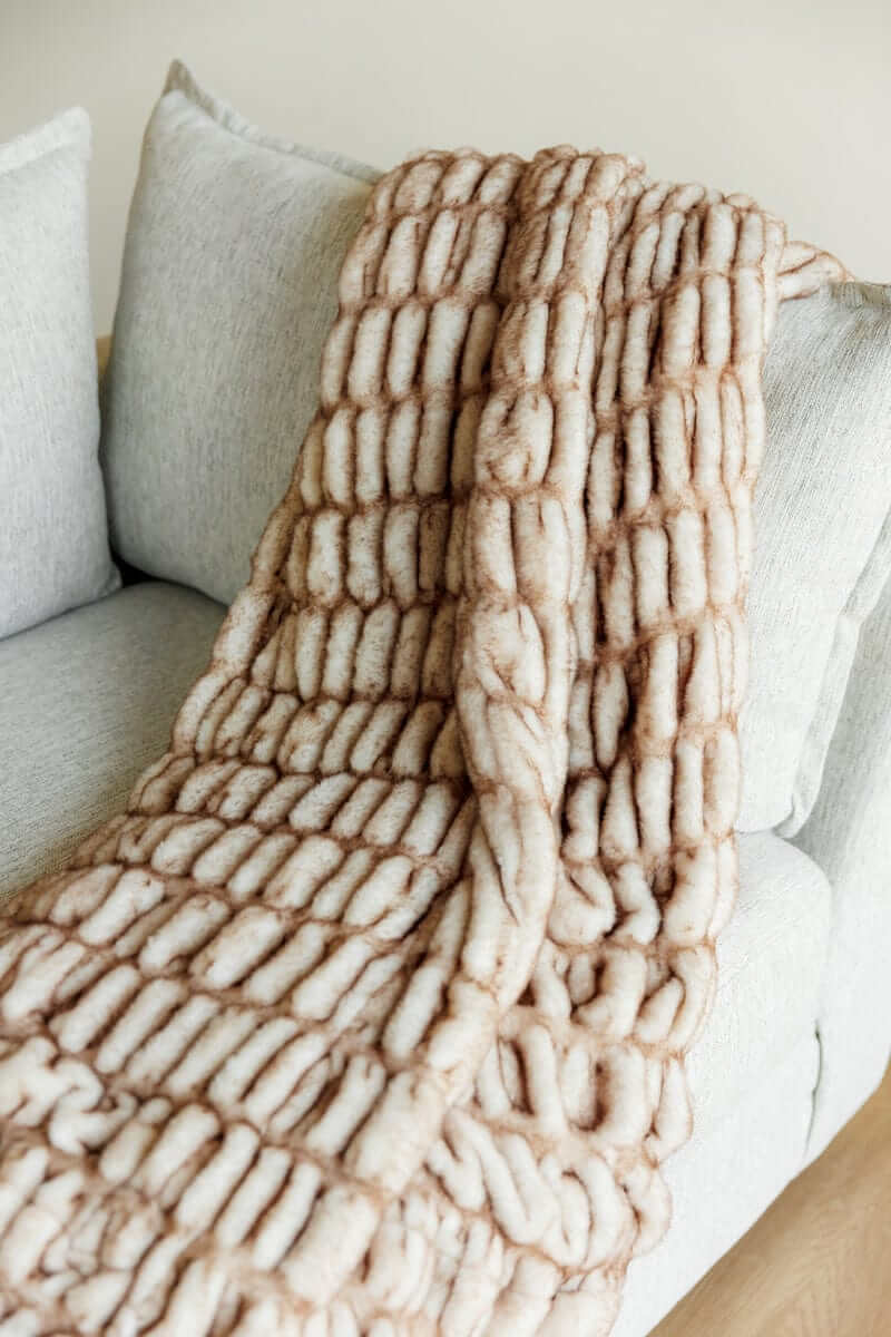 Hugs Topaz Blanket draped on a sofa, showcasing its cozy tan hue and plush and faux fur texture.