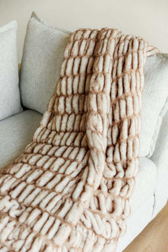 Hugs Topaz Blanket draped on a sofa, showcasing its cozy tan hue and plush and faux fur texture.