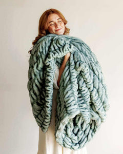 Hugs Jade Blanket wrapped around a woman, showcasing its plush, jade color and luxurious faux fur design.